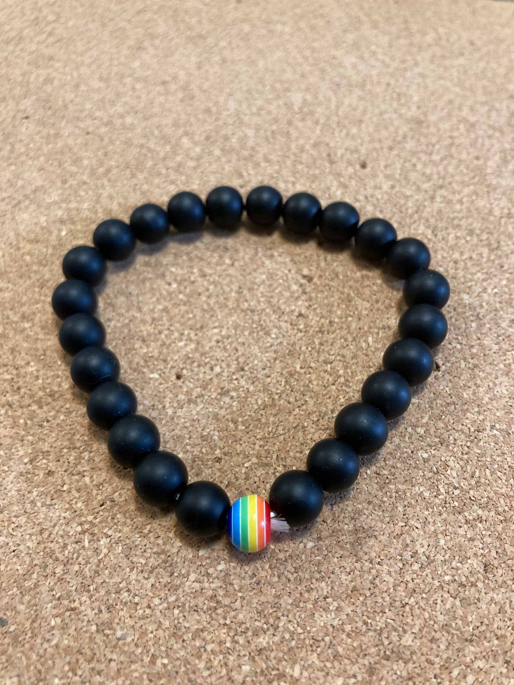 black beads with singular rainbow bead in the center. LGBTQ Pride